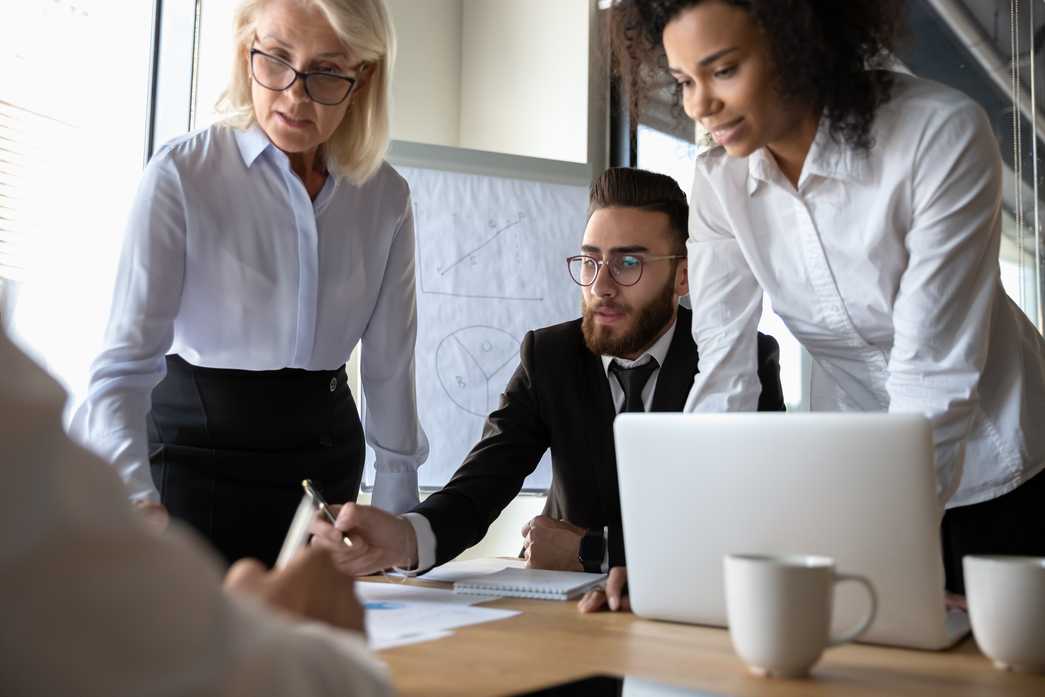Busy multi racial office workers brainstorming at group meeting in modern boardroom, focused professionals analysing data financial stats solving issues together in conference room, teamwork concept